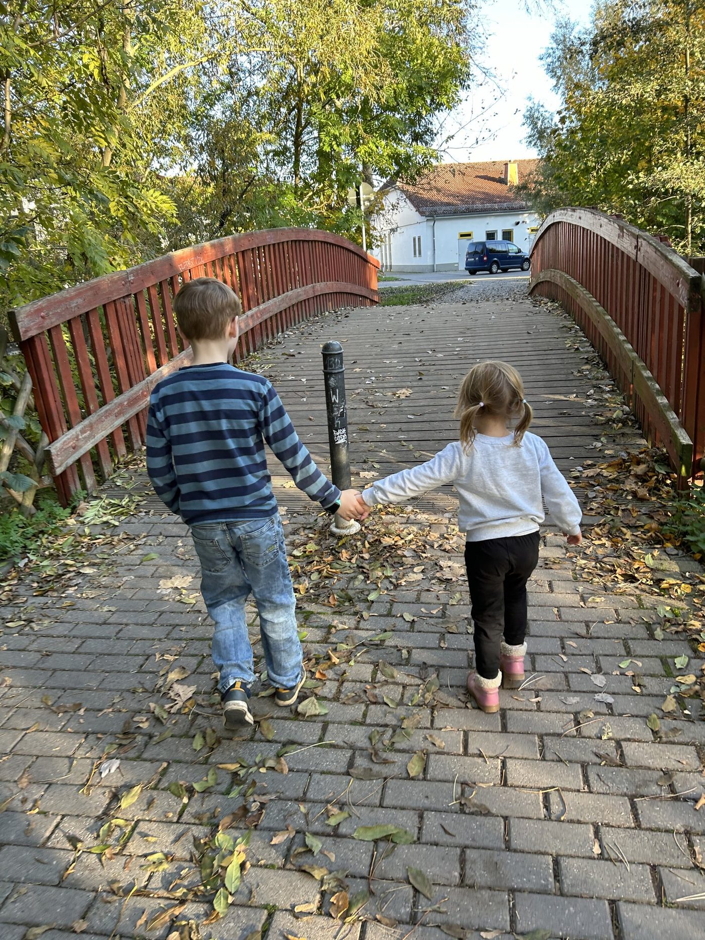 Zwei Kinder gehen Hand in Hand über eine hölzerne Brücke